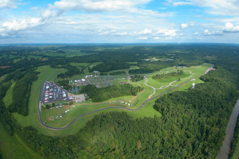 Aerial drone photo of virginia international raceway showing the whole property surrounded by green trees and grass with a blue sky and white clouds