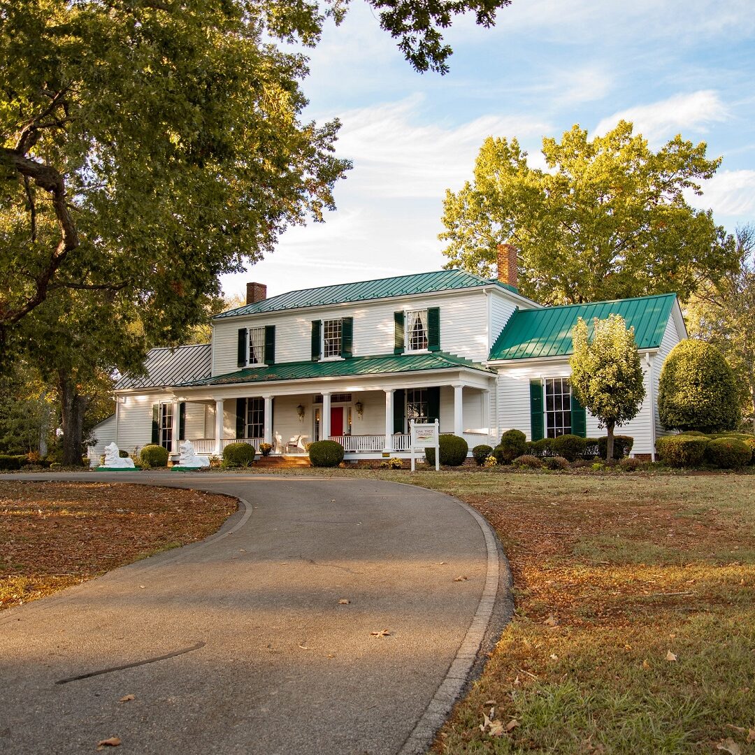 1800s white plantation house with a green roof, green shutters and a red door called the Oak Tree Tavern in the fall with orange leaves on the ground