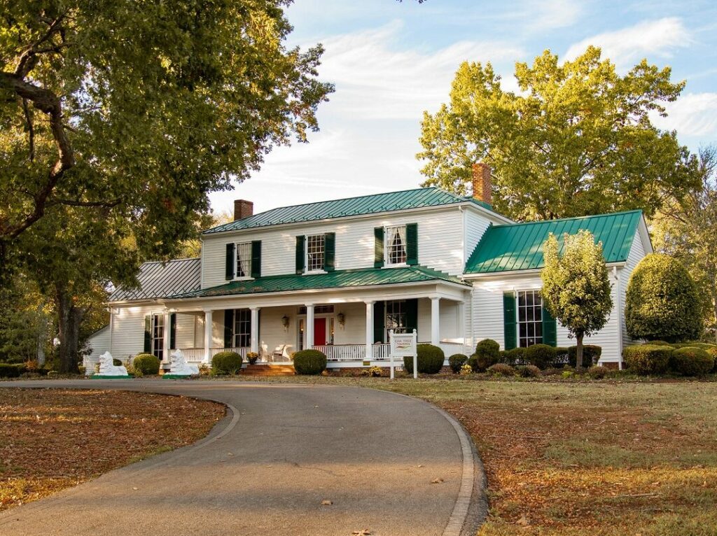 1800s white plantation house with a green roof, green shutters and a red door called the Oak Tree Tavern in the fall with orange leaves on the ground