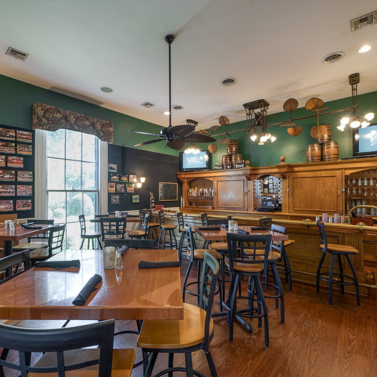 pub/bar with green walls and light brown wooden bar top with golden trim with wooden and black chairs and tables