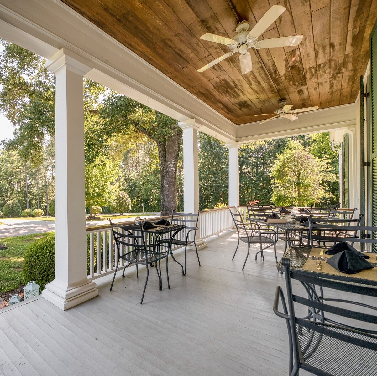 1800s plantation house front porch with grey painted boards and white railings with black chairs and tables