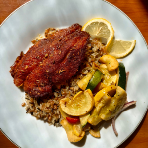 Baked fish on a bed of rice with a side of squash and zucchini on a white circle plate