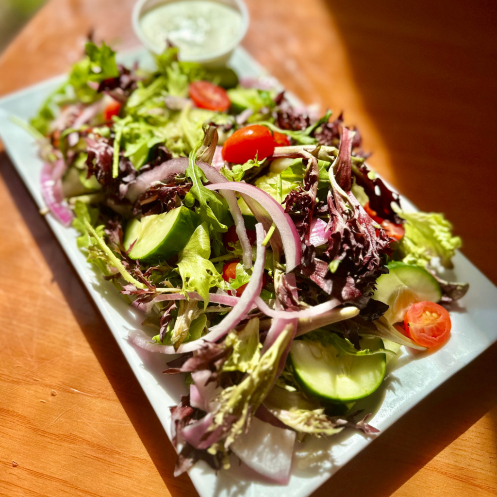 Salad with purple onions, cherry tomatoes and cucumbers with dressing on the side of a white rectangle plate