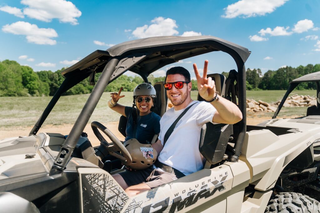 male and a female holding up the peace sign while sitting in a Yamaha wolverine RMAX atv side by side