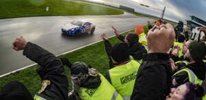 Operation Motorsports pit crew members wearing neon yellow vest clapping to their teams race car on track