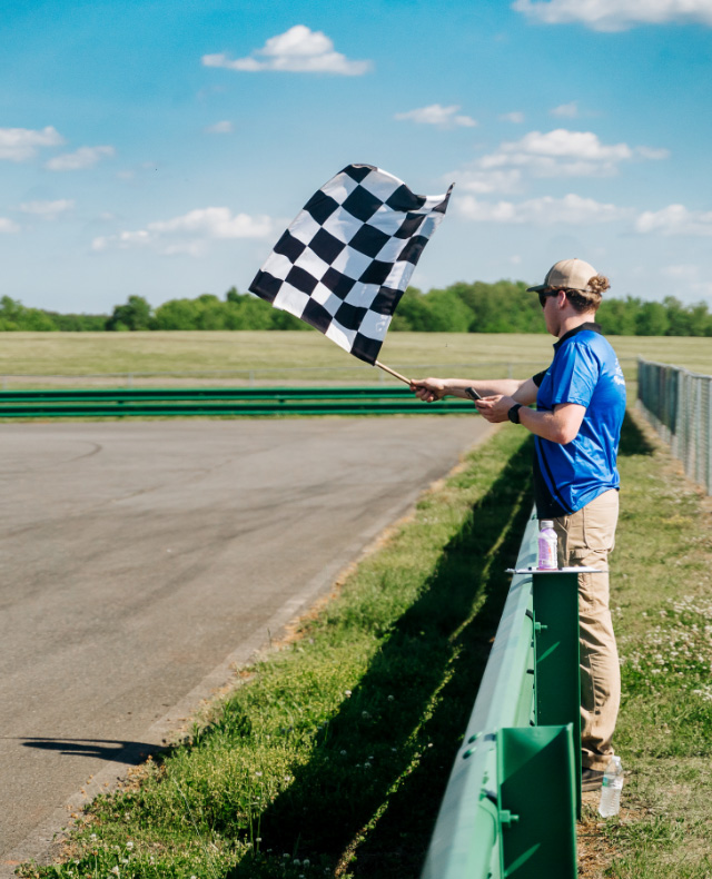 1 male wearing a blue polo shirt waving a black and white checkered flag at the VIR Skid Pad