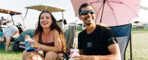 a man and woman sitting under an umbrella smiling watching a race