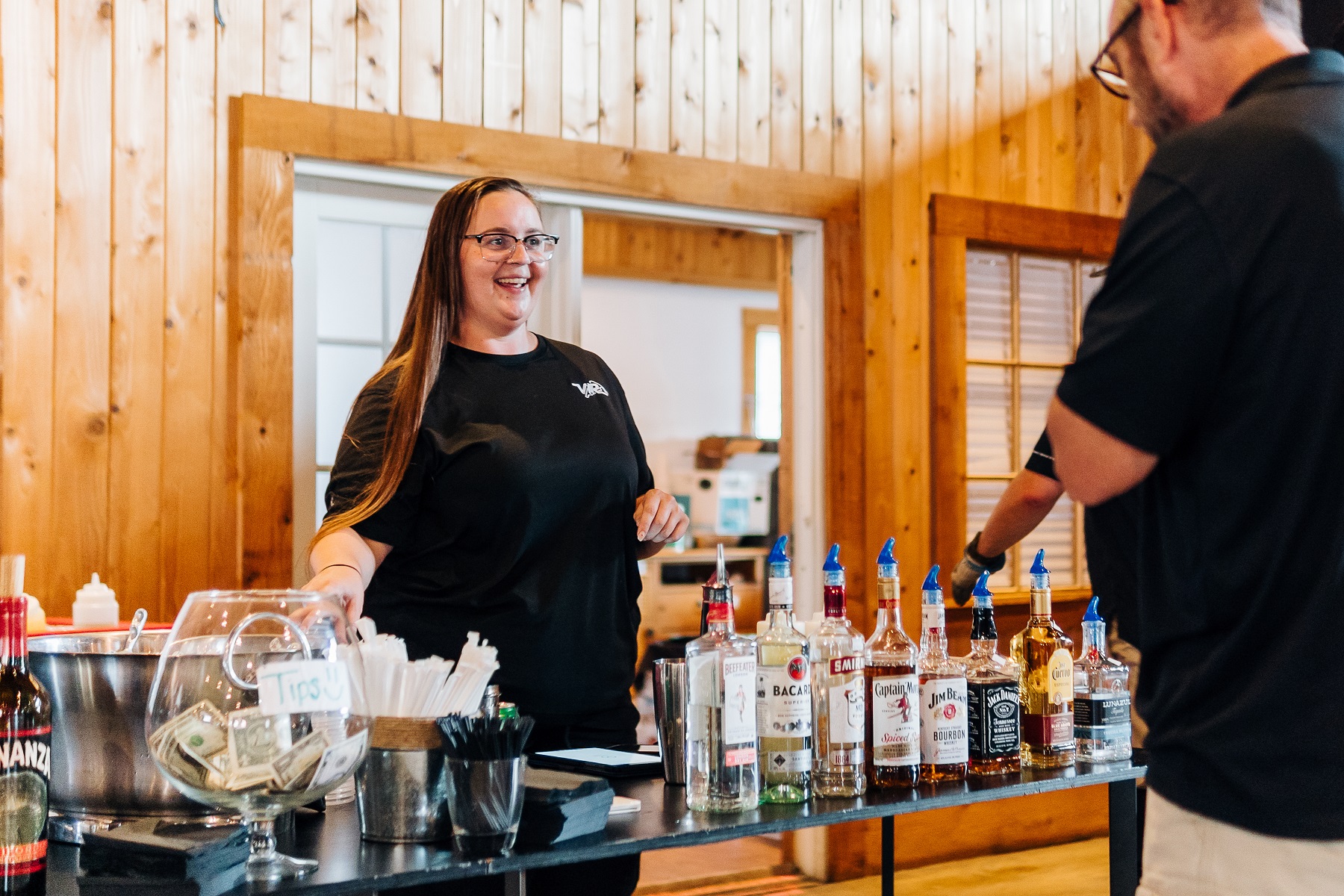 a woman standing behind a table with bottles of liquor