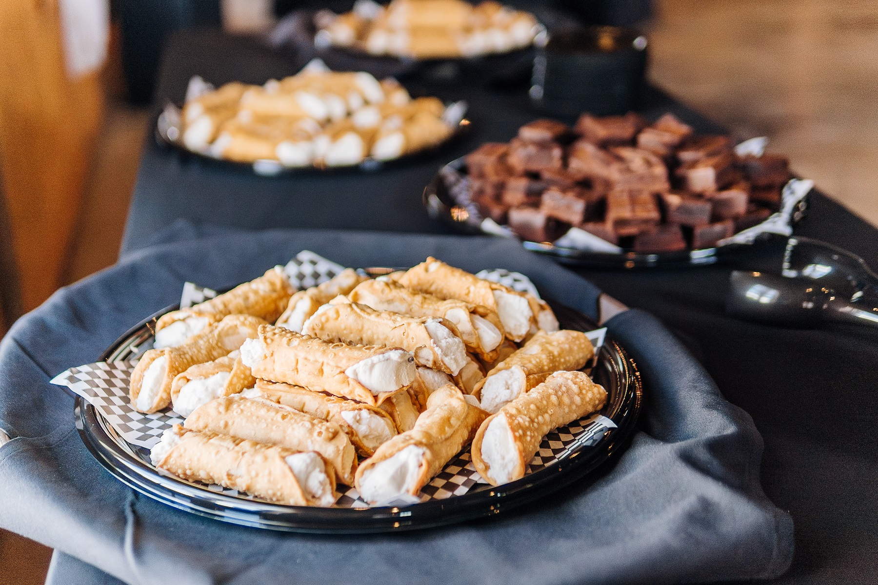 an assortment of desserts including cannolis and brownies on a black table