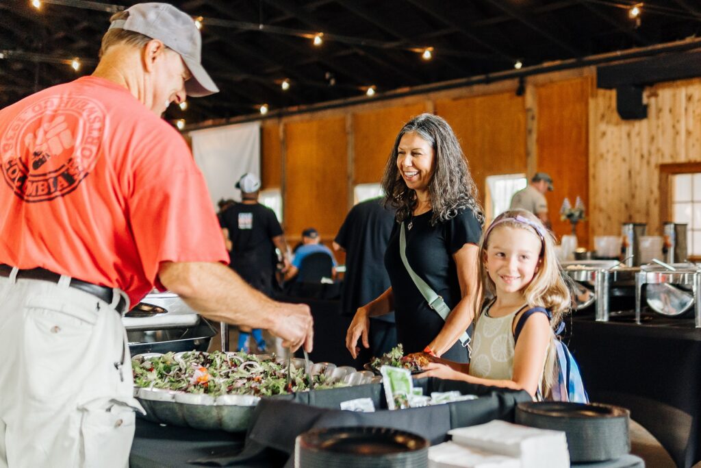 a man and woman standing and laughing by a food service table