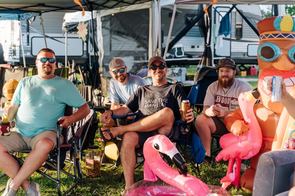 4 men sitting at campsite in camp chairs with drinks