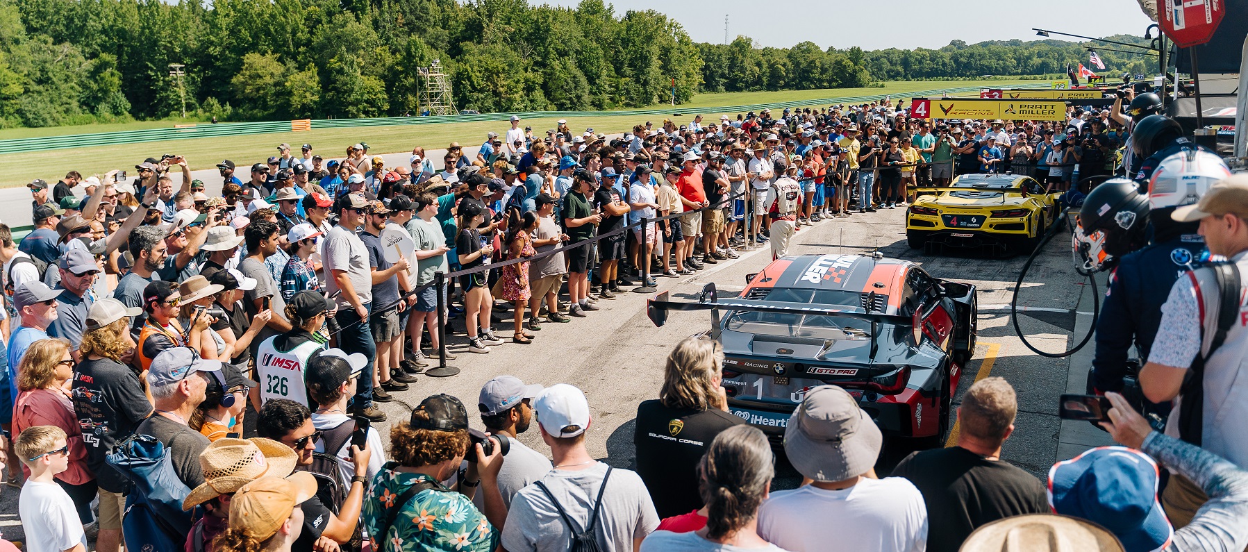 large group of people outside on a sunny day watching a racecar demonstration